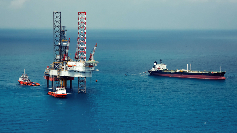 Zu sehen ist ein ruhiges, blaues Meer mit einer Ölbohrplattform, einem roten Versorgungsschiff und einem großen FPSO, das vorbeifährt.