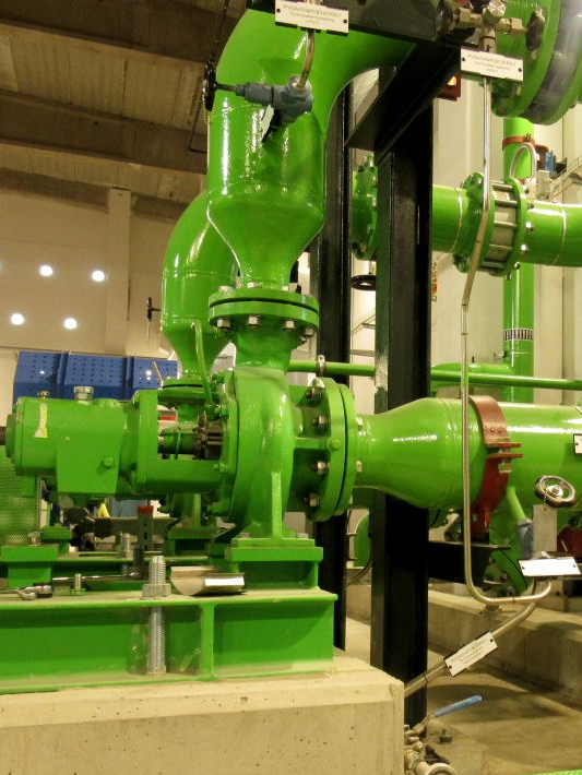Blick in ein Biomasse Herzkraftwerk auf eine einstufige Spiralgehäusepumpe mit geschlossenem Laufrad. Pumpenanlage und Verrohrungen sind leuchtend grün Lackiert und Pumpenaggregat ist auf einem Betonfundament befestigt. Im Hintergrund sind Hallenwände zu sehen.