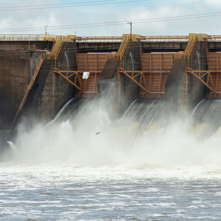 Die geöffneten Tore eines Wasserkraftwerks, durch die rauschende Wassermassen strömen.