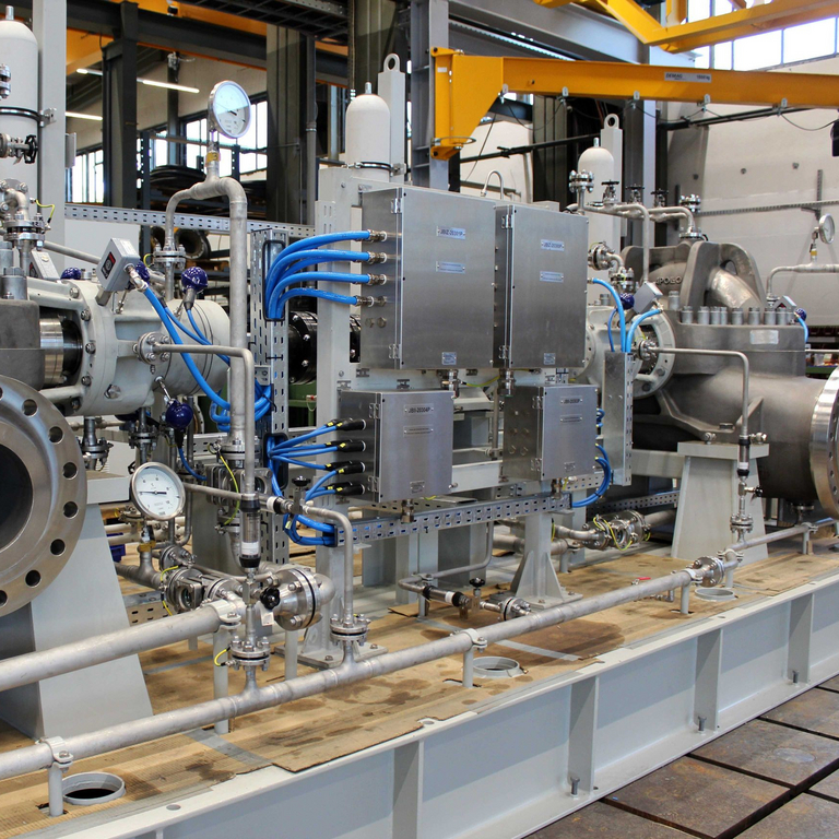 Ansicht auf das Hydraulic Power Recovery Turbine (HPRT) Aggregat mit einer BB1 Pumpe im Vordergrund, dann Verrohrung und Verkabelng mit Schaltkästen und nachfolgend eine ückwärts drehende, axial geteilte, einstufige Prozesspumpe des Typs ZMK (BB1 gemäß API 610).
