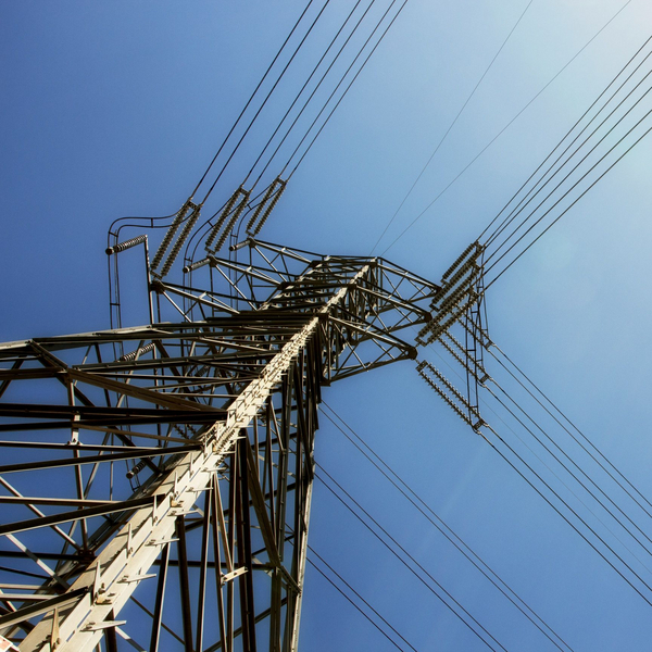 Der Blick von unten zeigt eine Stahlkonstruktion mit Stromleitung vor blauem, wolkenlosem Himmel bei Sonnenschein.