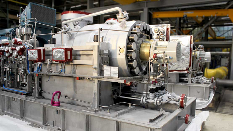 Seitenansicht einer TGD BB5 Liquid Export Barrelpumpe; robuste und massive Hochdruckpumpe für Offshore-Industrie, gefertigt in Deutschland nach API 610, Im Hintergrund sind Elementer einer Fertigungs- und Montagehalle zu erkennen.