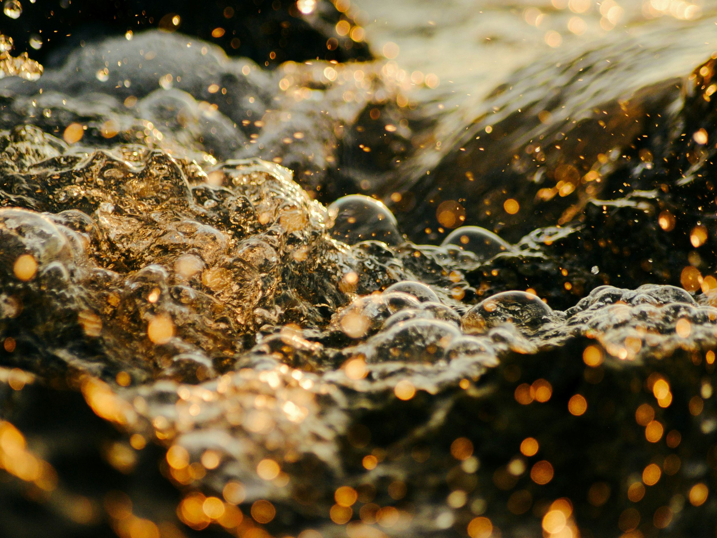 Es handelt sich um ein sprudelndes Wasser-Öl-Gemisch mit Luftblasen in einer leicht bräunlichen, orangen Farbe.